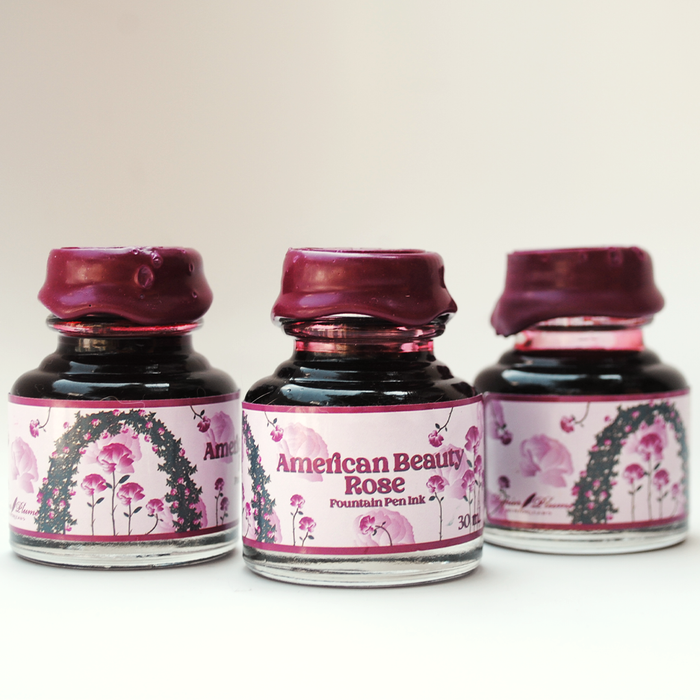 Papier Plume American Beauty Rose fountain pen ink in a glass bottle with vibrant pink and red ink, ideal for writing and calligraphy.