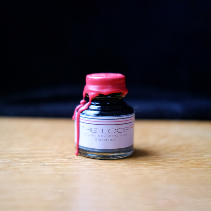 Green fountain pen ink from Papier Plume's Loop Series, shown in a clear bottle with a white cap.