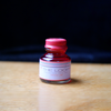 Bright orange Papier Plume Loop Series fountain pen ink bottle with a clear label and black cap.