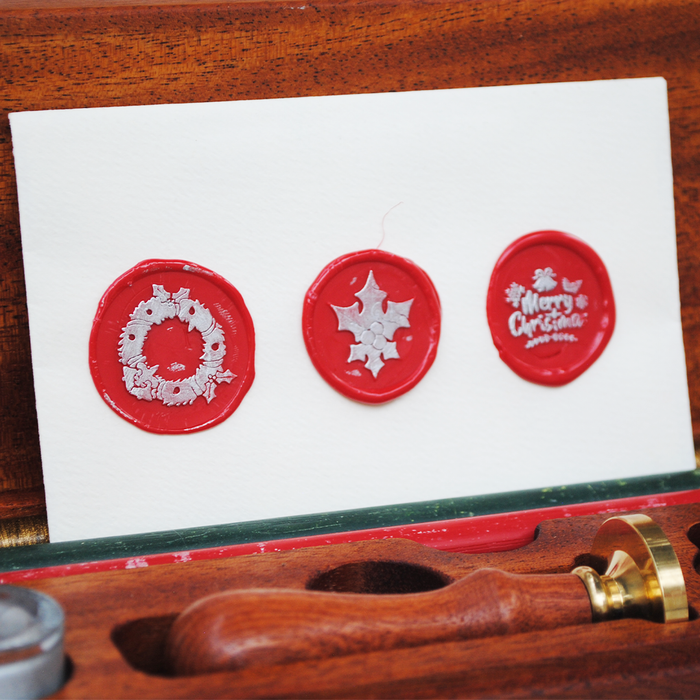 Set of red Christmas wax seals with Sliver designs on a white card, placed on a wooden surface.